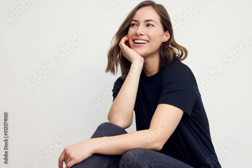 Portrait of a young happy woman smiling, looking beautiful and elegant. Sitting isolated on white background in a black t-shirt, looking casual.