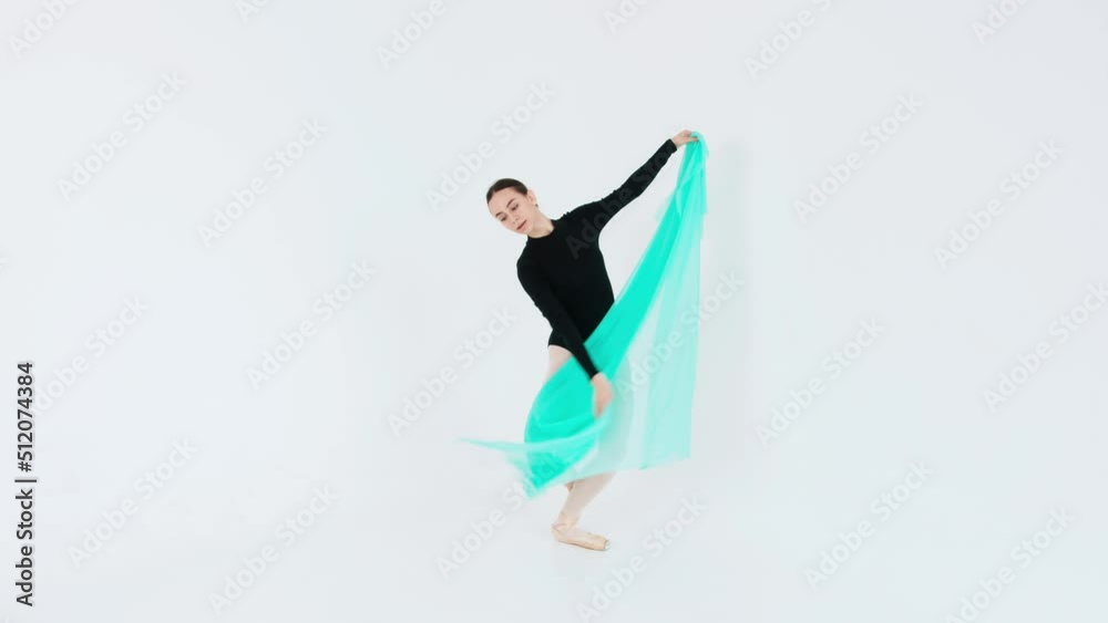 Charming ballerina demonstrates the elements of classical ballet with a bright translucent fabric in her hands in a white studio Charming ballerina demonstrates the elements of classical ballet with a bright translucent fabric in her hands in a white studio