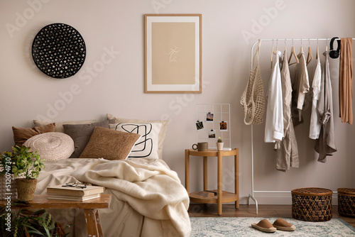 Stylish composition of cozy bedroom with mock up, beige bedding, and wooden armchair. Mock up poster with wooden frame. Home decor. Template.