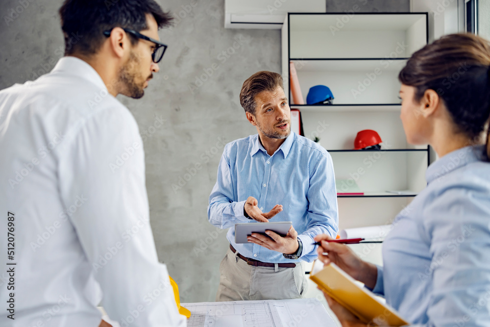 Obraz premium A main architect manages project on tablet in the office and talking to the colleagues.