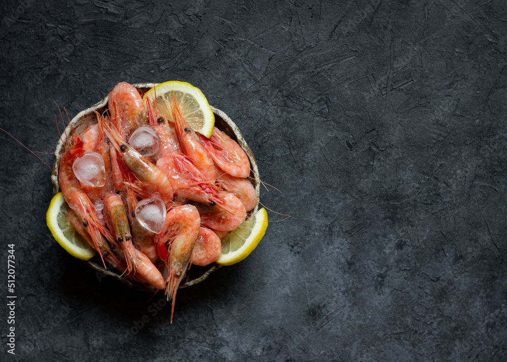 Raw shrimps with lemon and ice on a dark background.