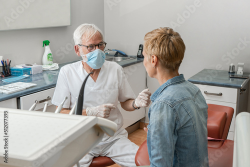 Mature experienced male doctor in glasses and face mask consulting the patient at dental clinic. Doctoral practice. Patient healthcare