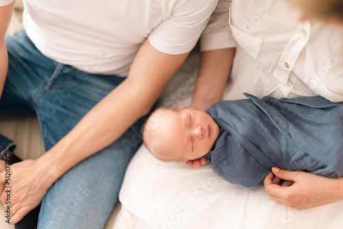 Close-up of parents holding newborn baby son wrapped in swaddle blanket at home.