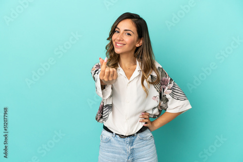 Young woman over isolated blue background making money gesture