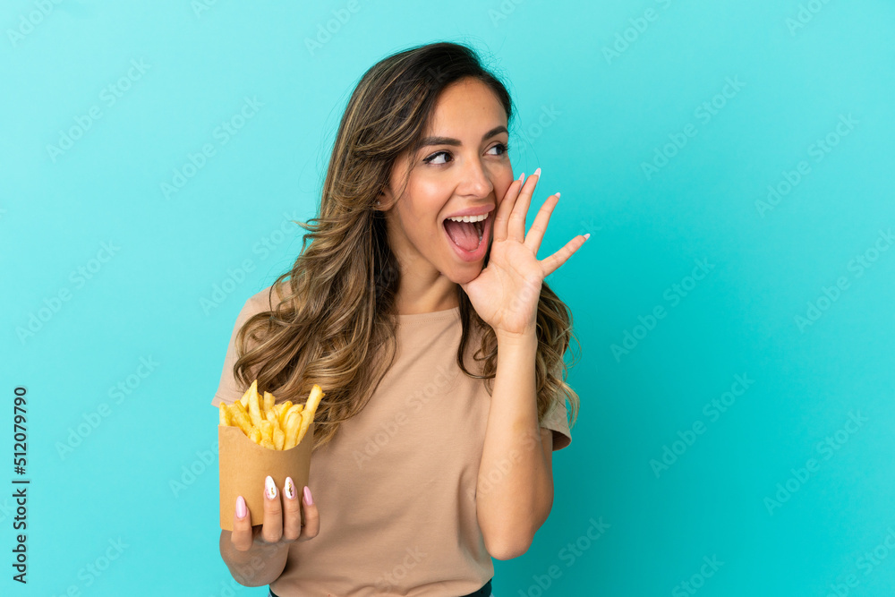 Young woman holding fried chips over isolated background shouting with mouth wide open to the side Young woman holding fried chips over isolated background shouting with mouth wide open to the side