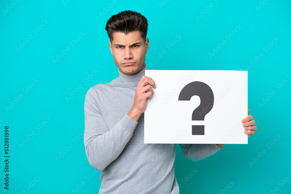 Young handsome caucasian man isolated on blue bakcground holding a placard with question mark symbol with sad expression Young handsome caucasian man isolated on blue bakcground holding a placard with question mark symbol with sad expression