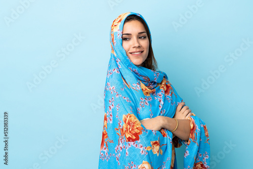 Young Moroccan woman with traditional costume isolated on blue background with arms crossed and happy