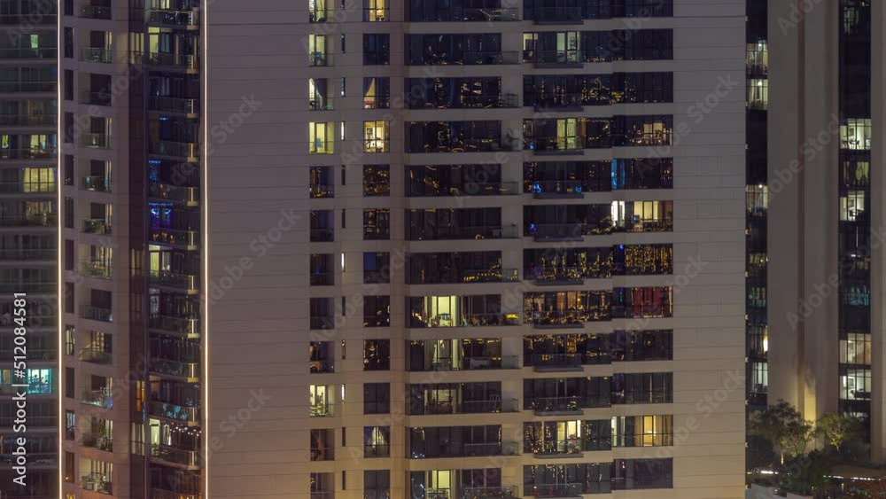 Windows illuminated at night in modern residential buildings timelapse. Multi-level skyscrapers with many glowing lights.