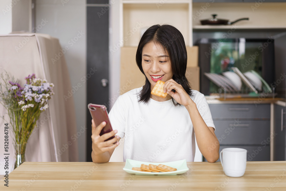 Home relaxation concept, Young woman eating crackers and surf social media on smartphone at home Home relaxation concept, Young woman eating crackers and surf social media on smartphone at home