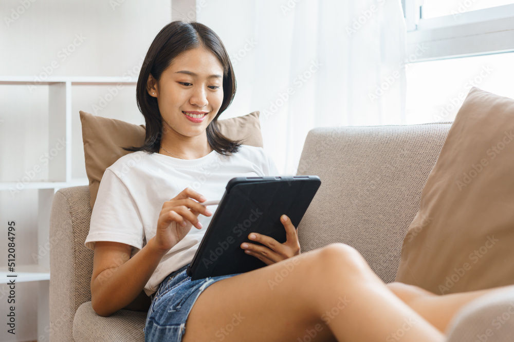 Cozy lifestyle concept, Young woman lying on couch and using tablet to surf social media at home Cozy lifestyle concept, Young woman lying on couch and using tablet to surf social media at home