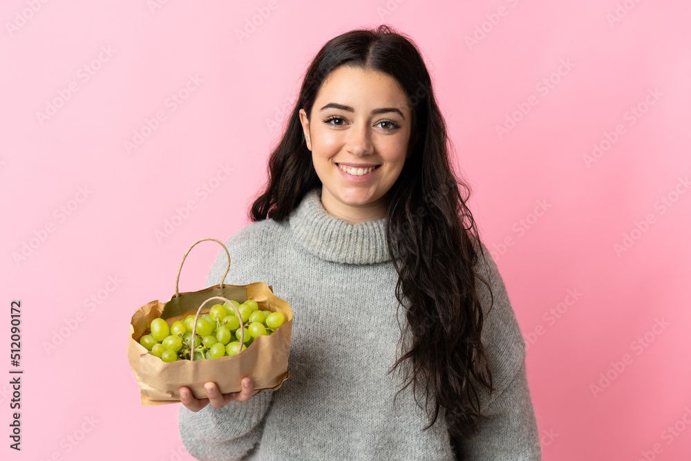 Young caucasian woman holding a grapes isolated on blue background smiling a lot Young caucasian woman holding a grapes isolated on blue background smiling a lot