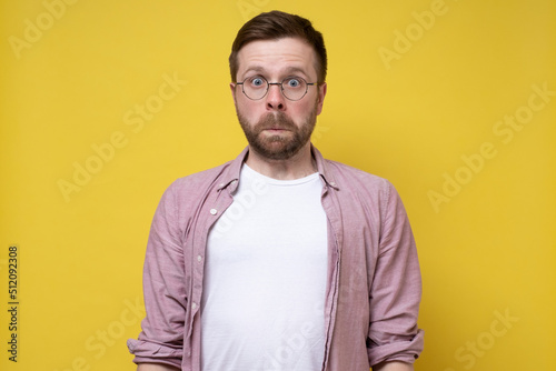 Man with glasses in a stupor stands motionless, he is frightened and shocked. Yellow background.