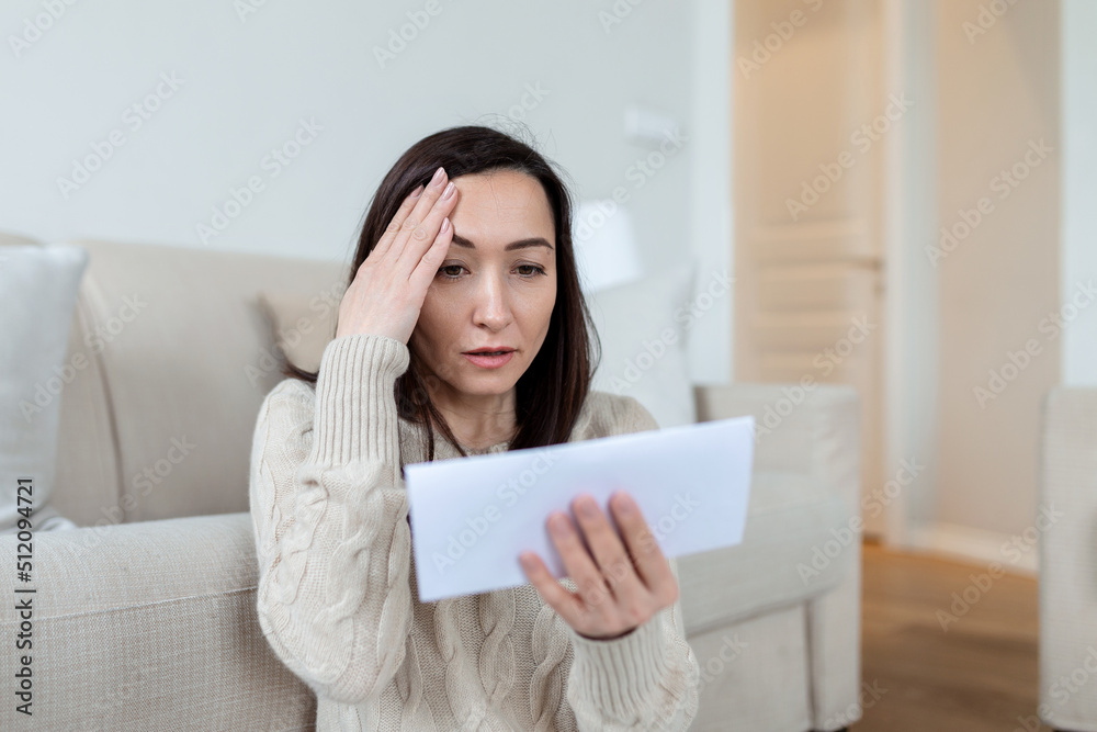 Portrait of a worried Asian woman looking at received letter at home. Beautiful woman with worried facial expression looking at received mail. Portrait of a worried Asian woman looking at received letter at home. Beautiful woman with worried facial expression looking at received mail.