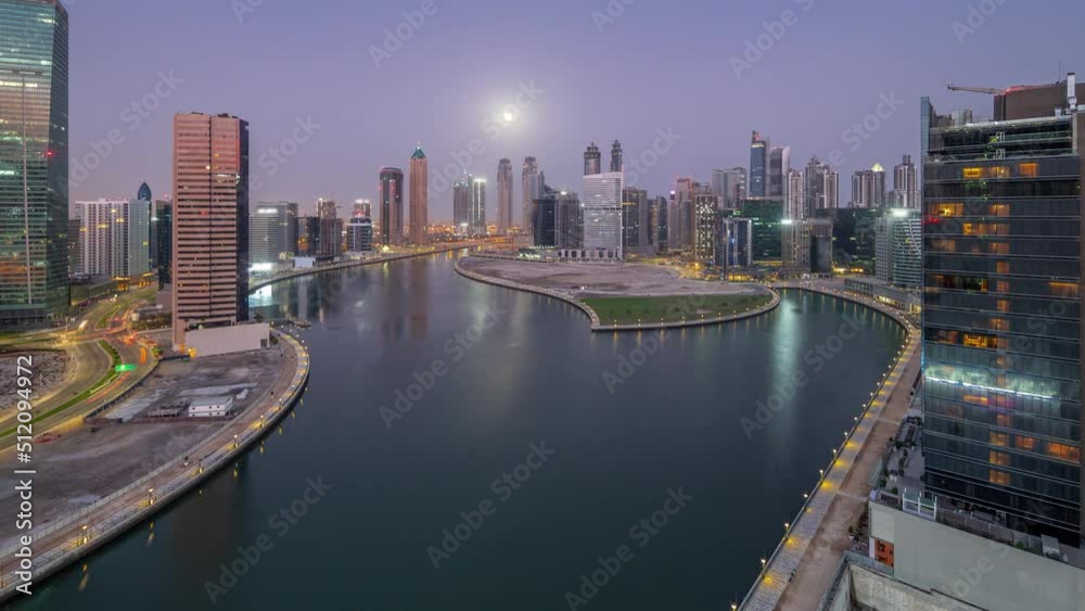 Cityscape of skyscrapers in Dubai Business Bay with water canal aerial night to day transition timelapse with Moon setting down. Modern skyline with illuminated towers and waterfront before sunrise Cityscape of skyscrapers in Dubai Business Bay with water canal aerial night to day transition timelapse with Moon setting down. Modern skyline with illuminated towers and waterfront before sunrise