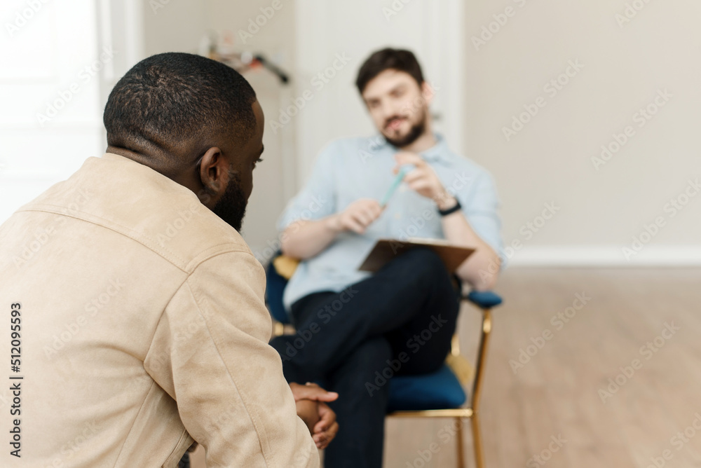 Unhappy young black man having session with professional psychologist at mental health clinic. Professional psychological help concept.