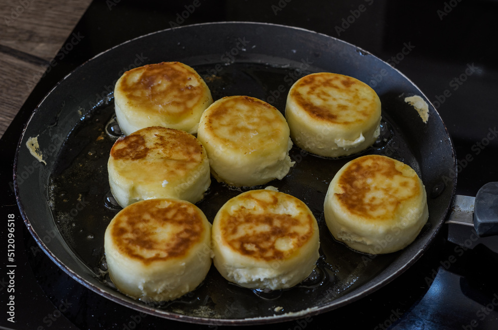 The cook prepares a morning breakfast, syrniki in a frying pan on an induction stove The cook prepares a morning breakfast, syrniki in a frying pan on an induction stove