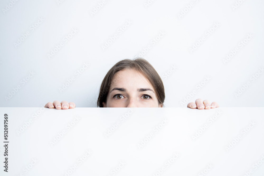 Young woman looking to the side looking out from under a white table against a white wall Young woman looking to the side looking out from under a white table against a white wall