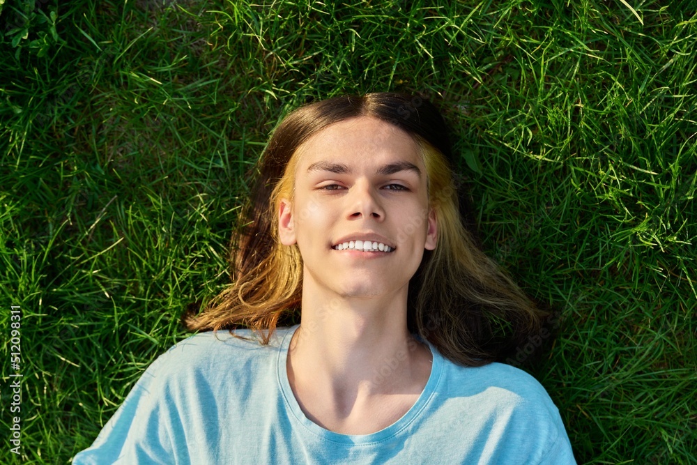Smiling young guy looking at the camera, lying on the grass Smiling young guy looking at the camera, lying on the grass