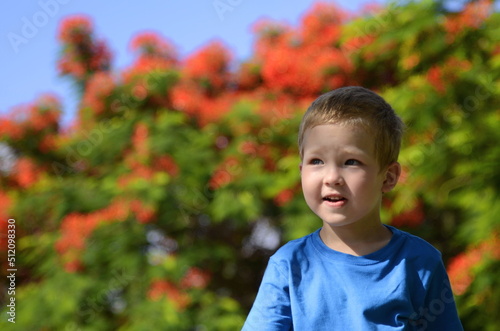 Portrait of a little boy on the background of a flowering tree. The child is blond, emotions on his face. Concept: traveling with children, advertising a kindergarten, a children's camp.