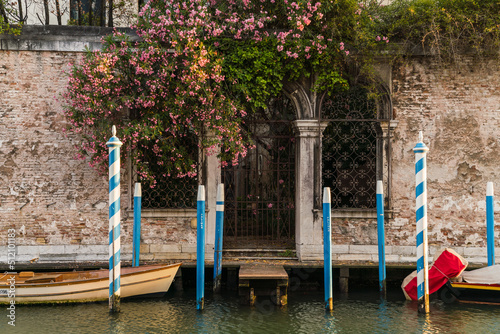 Charming facade in Venice, Italy with pink flowers hanging over and boat docked
