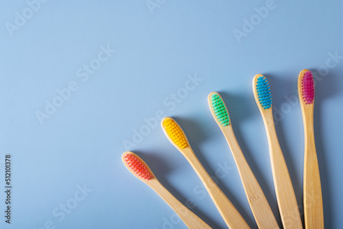 Five bamboo toothbrushes with multi-colored bristles on a blue background