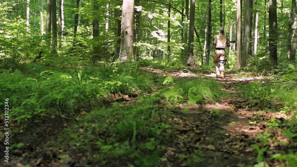 military soldier runs through the forest with a machine gun and a pistol in a holster on his leg. a soldier in uniform with a bulletproof vest runs through the forest. back view military soldier runs through the forest with a machine gun and a pistol in a holster on his leg. a soldier in uniform with a bulletproof vest runs through the forest. back view