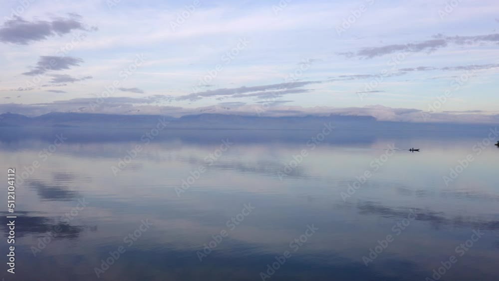 Isolated fisherman boat in silent waters of lake reflecting the cloudy sky and small island in middle. Isolated fisherman boat in silent waters of lake reflecting the cloudy sky and small island in middle.