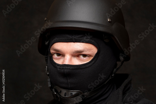 Portrait of a military soldier in a bulletproof vest and balaclava, army helmet on his head, black background. Concept: volunteer at war, war in Ukraine, civil self-defense, army unit. © Anelo