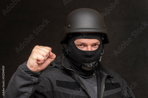 Portrait of a military soldier clutching his fist, wearing a bulletproof vest and balaclava, army helmet on his head, black background. Concept: volunteer at war, war in Ukraine, civil self-defense, © Anelo