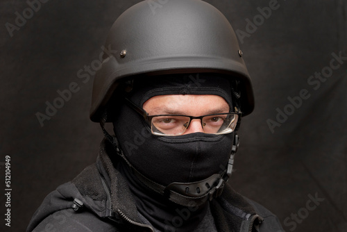 Portrait of a military man with glasses, wearing a bulletproof vest and balaclava, an army helmet on his head, black background. Concept: military journalist, volunteer at war, war in Ukraine. © Anelo