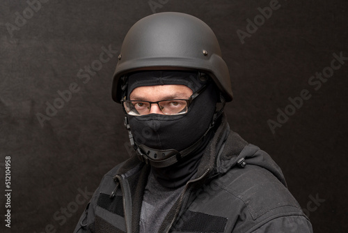 Portrait of a military man with glasses, wearing a bulletproof vest and balaclava, an army helmet on his head, black background. Concept: military journalist, volunteer at war, war in Ukraine. © Anelo