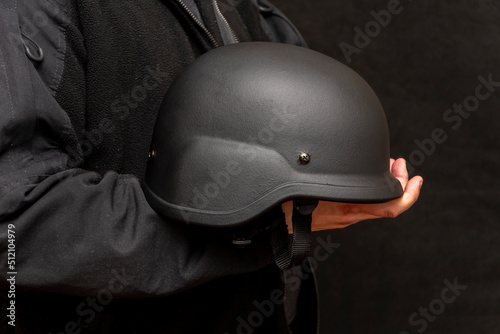 A military man holds an army helmet in his hand, black background. Concept: volunteer at war, war in Ukraine, civil self-defense, army unit.