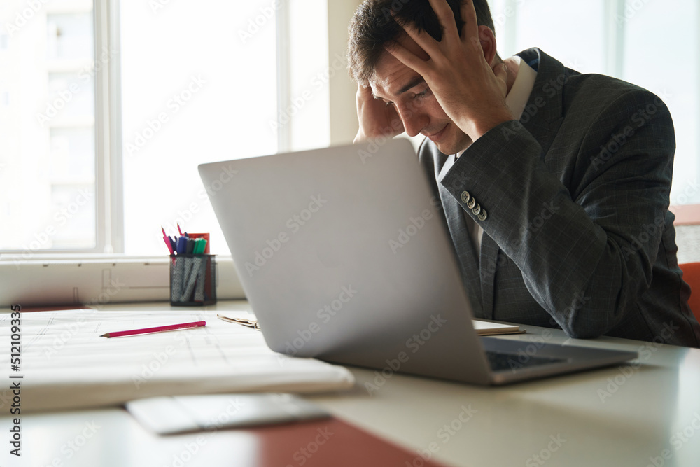 Stressed worker grabbing his head during work on laptop Stressed worker grabbing his head during work on laptop