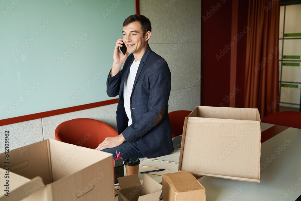 Worker answering the call while sitting on table among boxes Worker answering the call while sitting on table among boxes