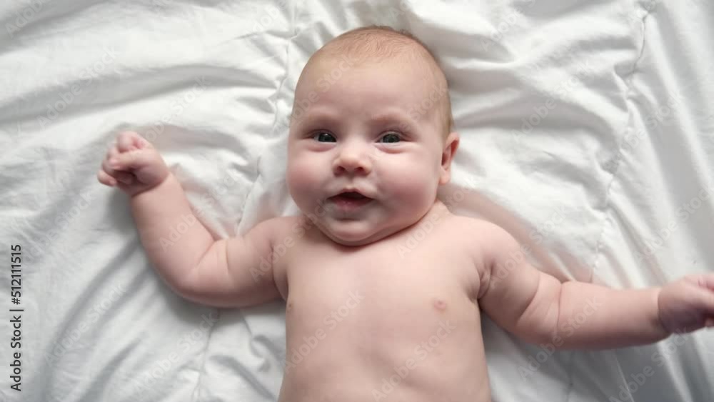 Happy naked baby in diaper lying on his back on the white sheet and touching his face. Baby girl with red hair looking at camera. Light background. Little child. Serious emotion. Advertising Mockup Happy naked baby in diaper lying on his back on the white sheet and touching his face. Baby girl with red hair looking at camera. Light background. Little child. Serious emotion. Advertising Mockup