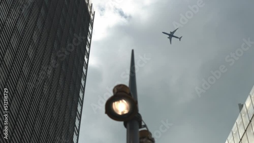 Airplane Flight Over Business Center Of Skyscrapers At London. Bottom View Of High-rise Buildings With Flying Plane In Blue Sky With Clouds in Afternoon. Air Transport, Travel, Vocation concept.