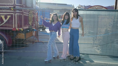 Three smiling girls by metal fence lift their roller skates, push-in photo