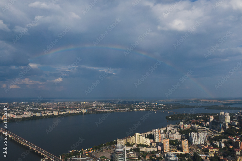 Beautiful rainbow after the rain on the blue sky and clouds over the city. An amazing natural phenomenon when sunlight is combined with rain. Photo taken from a drone