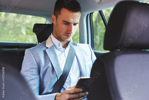 A businessman with a tablet sits in the back seat of a car and works