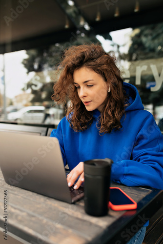 Obraz na płótnie Focused caucasian woman working with computer at table outdoor in spring day. Brunette looks displeased at notebook screen. Freelance work, business people concept w salonie