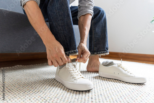 Man tie the shoelace of white sneakers sit on wood bench at home.