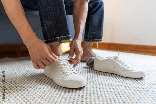 Man tie the shoelace of white sneakers sit on wood bench at home.
