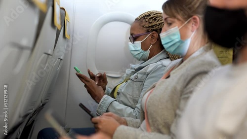 Multiracial people sitting inside aircraft using mobile phone while wearing safety face masks for coronaviurs outbreak
 photo