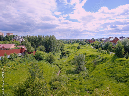 The valley of a small river surrounded by green hills and lush farmland with red cottages in the warm rays of the sun. Russia. Moscow oblast. The city of Chekhov.