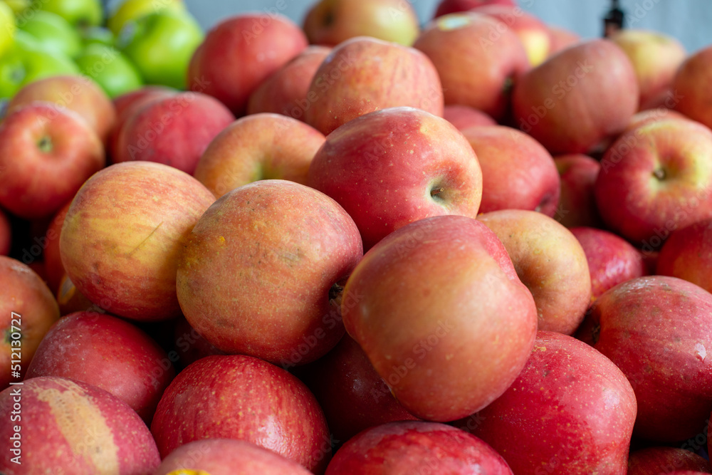 A stack or bulk supply of large red ripe Fuji apples on a table for sale at a farmer's market. There are green granny smith apples in the background. The red organic apples are fresh sweet produce. A stack or bulk supply of large red ripe Fuji apples on a table for sale at a farmer's market. There are green granny smith apples in the background. The red organic apples are fresh sweet produce.
