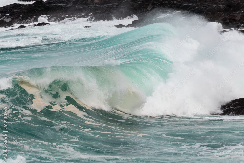 An angry teal green color massive rip curl of a wave as it barrels rolls along the ocean. The white mist and froth from the wave are foamy and fluffy. The ocean spray is coming off the top of the wave An angry teal green color massive rip curl of a wave as it barrels rolls along the ocean. The white mist and froth from the wave are foamy and fluffy. The ocean spray is coming off the top of the wave