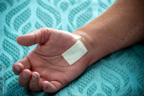 A female nurse removes a padded bandage on the wrist and hand of a woman. The palm has a number of black nylon stitches from a recent carpal tunnel surgery. The wound is closed with no infection. 