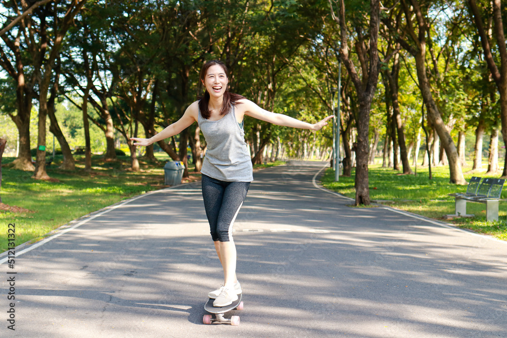 Asian woman exercising in the morning Practice basic skateboarding on the streets of the park. Playing sports for health makes you strong and happy.