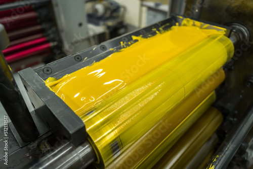 Yellow ink in the paint system compartment of a modern flexographic printing press in a print shop. Yellow paint in the ink feeder on the printing cylinder. Selective focus photo