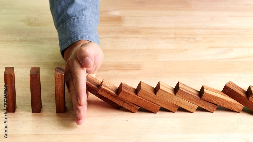 Business crisis, risk management concept, businessman hand stopping or preventing falling dominos effect of risk, business crisis on wooden table, slow motion